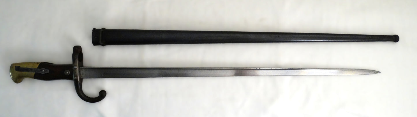 Baïonnette Gras modèle 1874 avec poignée laiton et noyer, croisière à quillon et fourreau bronzé. Lame marquée Saint-Étienne, pièce originale de l’époque IIIᵉ République. Vue complète coté droit.