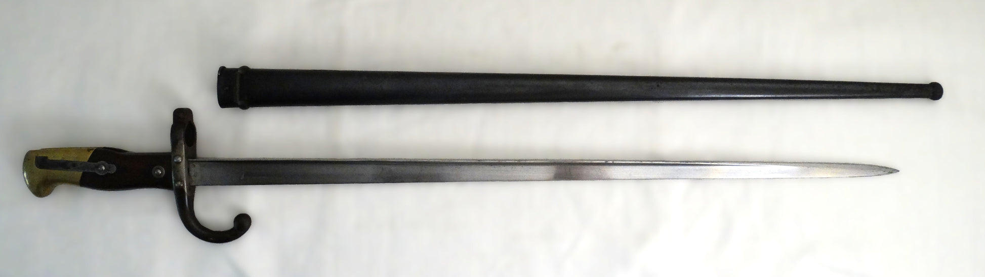 Baïonnette Gras modèle 1874 avec poignée laiton et noyer, croisière à quillon et fourreau bronzé. Lame marquée Saint-Étienne, pièce originale de l’époque IIIᵉ République. Vue complète coté droit.